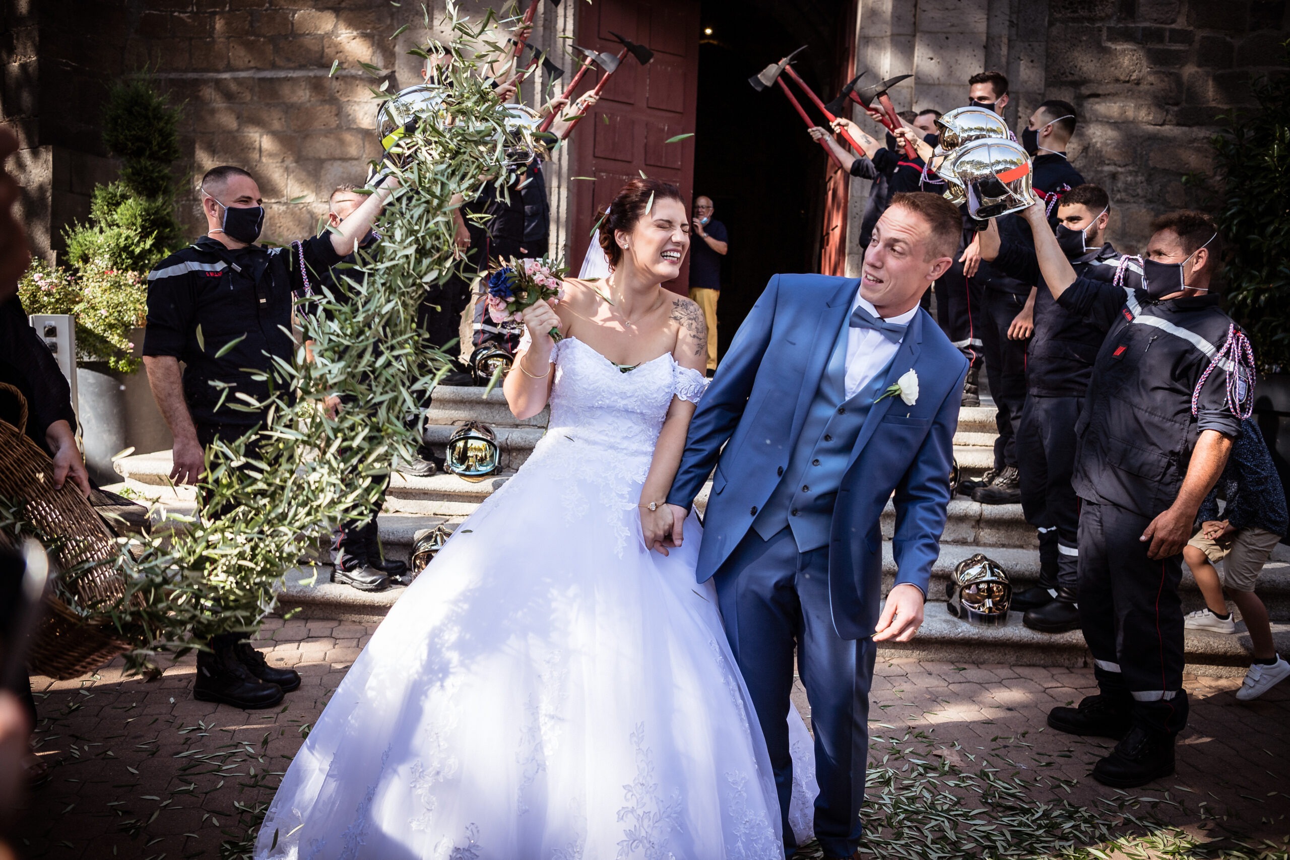 Cout d'un photographe. Sortie d'église des mariées avec une haie d'honneur des pompiers. Les mariées se prennent des feuilles d'olivier.